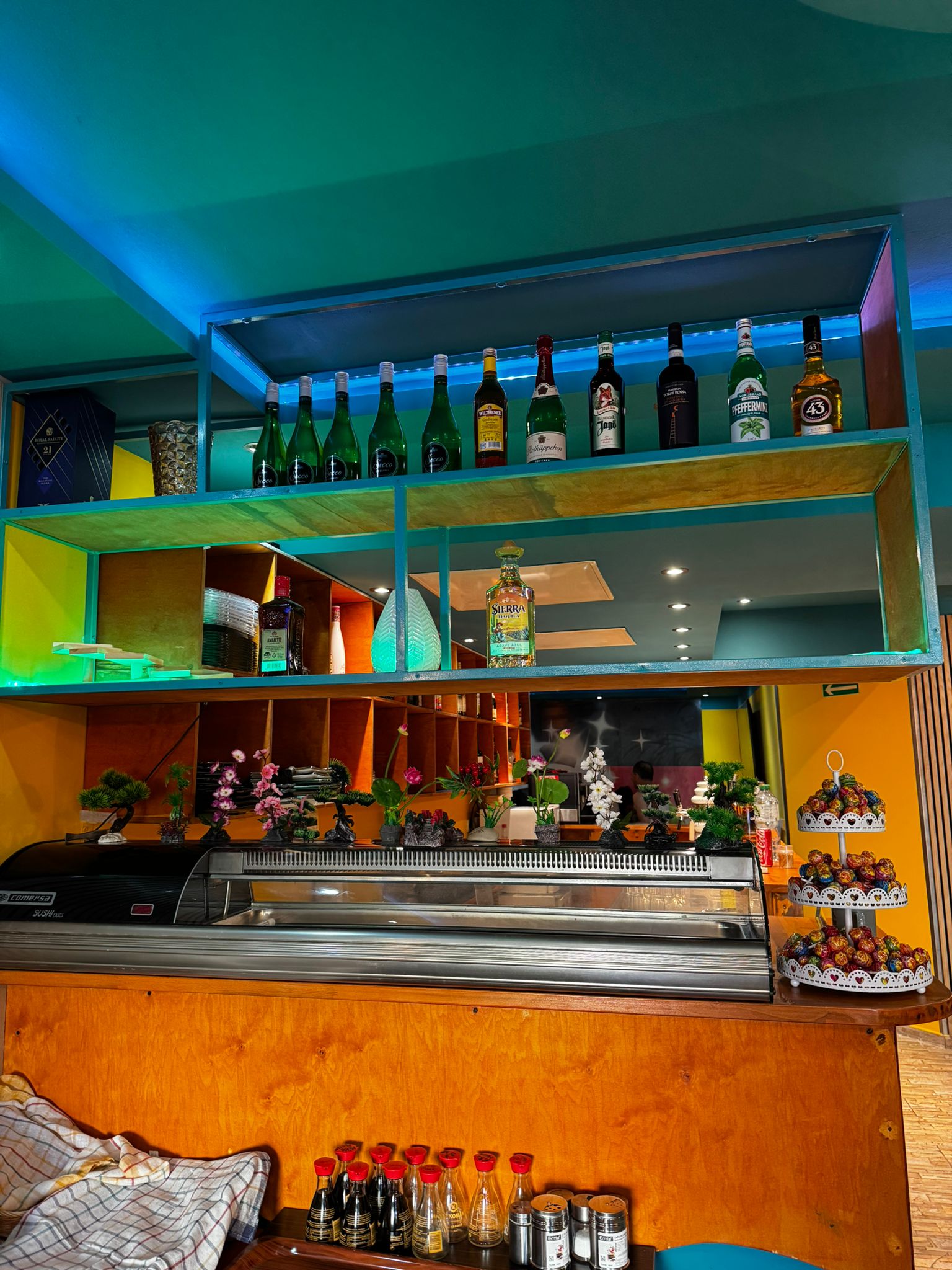 Detailansicht der Bar mit Sushi-Vitrine, Spirituosen-Regalen und türkiser Deckenbeleuchtung